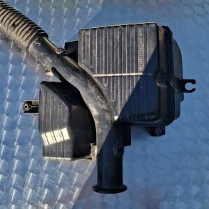 Front view of a black plastic air filter housing for Honda Ballade 1500 displayed on a grey surface.Front view