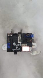 Used fusebox unit for 2009 Mazda 2 shown from front angle with visible wiring and connectors.Used fusebox unit