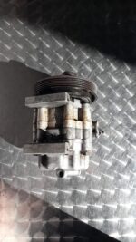 Front view of a car aircon pump showing mounting points and pulley system in bright lighting.Front view of a c
