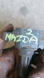 Close-up of a black Mazda 2 pencil coil positioned upright on a plain surface, new condition.Close-up of a bla