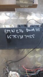 Front-angle view of BMW control unit for alarm system, showing connector pins and black casing.Front-angle vie