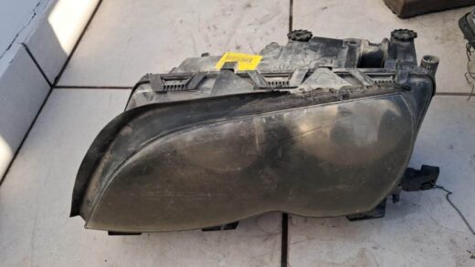A used car headlight assembly lying on a tiled surface, showing a cloudy lens and visible wear and dirt.