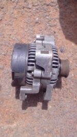 Front angled view of a used alternator for Volvo V90 showing mounting points and electrical connectors.Front a