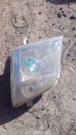 Front view of a used left headlight for an Isuzu KB, showing clear lens and mounting bracket details.Front vie