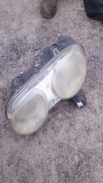 Left side car headlight assembly shown from front angle, used condition visible with slight wear.Left side car