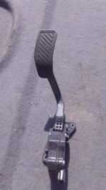 Close-up of a used accelerator pedal positioned upright against a plain background.Close-up of a used accelera