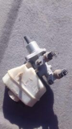Used brake master cylinder shown from a side angle with connected reservoirs and mounting points.Used brake ma