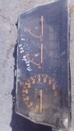 Front view of a used Mazda 323 dashboard instrument cluster showing gauges and indicator lights.Front view of