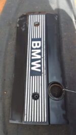 Front view of used BMW 3.0 engine cover resting on a blue surface, showing mounting points and details.Front v