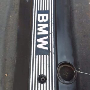 Front view of used BMW 3.0 engine cover resting on a blue surface, showing mounting points and details.Front v