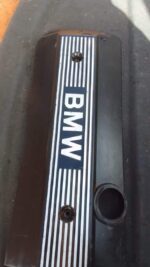 Top-down view of a used black BMW E46 engine cover with silver accents and visible mounting points.Top-down vi