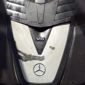 Used V6 engine cover viewed from top front angle, showing mounting points and Mercedes emblem.Used V6 engine c