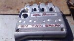 Top-down view of a used Twin Spark 16V engine cover showing the Alfa Romeo logo and mounting points.Top-down v