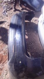 Rear view of a used Infiniti FX37 rear bumper displayed flat on a surface with minor wear visible.Rear view of