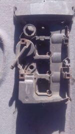 Front angled view of a used black tappet cover for Mercedes W203 engine on a white background.Front angled vie