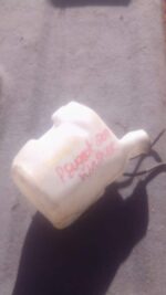 Front view of a used washer bottle for Peugeot 207, showing the container and attached hose.Front view of a us