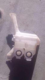 Used washer bottle for a 2009 Toyota Yaris, shown from the front with attached fluid cap and hose.Used washer
