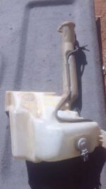 Front angled view of a used Jeep Cherokee windshield washer bottle with attached hose and pump assembly.Front