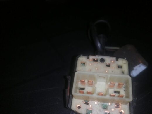 Close-up view of a multi-pin electrical connector with several copper contacts and a black background, showing a portion of a connecting cable.