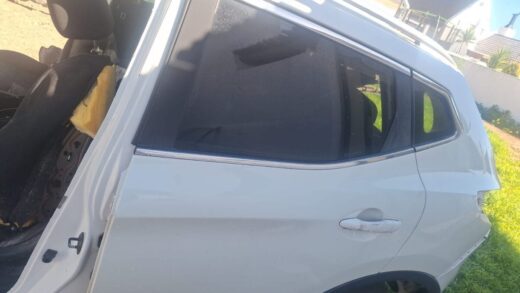 Whatsapp Image 2025-06-21 At 12.24.51 A side view of a white vehicle, showing the rear door and window with tinted glass, partially revealing the interior which has a seat with torn upholstery. The background consists of grass and a house.