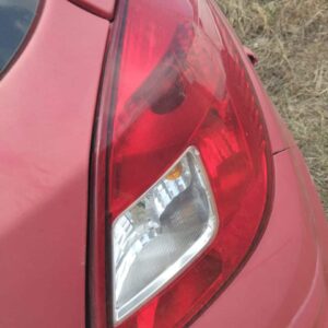 Close-up of a red car's rear tail light, featuring a clear lens section and a red plastic cover, set against a backdrop of dry grass.
