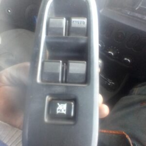 A hand holding a vehicle window control switch with three buttons: two for window operation marked with a textured surface and an 'AUTO' label, and a third button with a symbol indicating a lock or disabled feature, set against a blurred background of a vehicle interior.