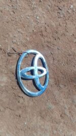 Front view of a used Toyota car badge emblem with some wear visible on the surface.Front view of a used Toyota